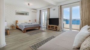 Έ να υπνοδωμάτιο με ένα κρεβάτι, μια τηλεόραση, ένα μπαλκόνι με θέα και έναν λευκό τοίχο από τούβλα.