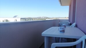 Ein Balkon mit Tisch und Stühlen, einer weißen Tasse und Blick auf entfernte Gebäude und Berge.