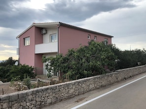 Ein zweistöckiges Gebäude mit rosafarbenem Mauerwerk, einem Balkon und einer Steinwand davor.