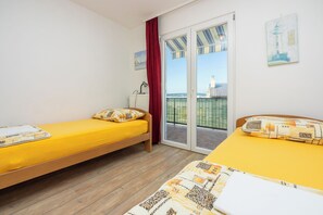 A room with two beds, a radiator, a window with curtains, and a view of a lighthouse. - Apartment Klemi (Crikvenica)