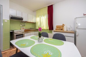 A compact kitchen with a dining table, chairs, a stove, oven, and a refrigerator. - Apartment Klemi (Crikvenica)