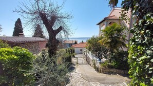 A stone pathway leading to a building with a tiled roof, surrounded by greenery and a clear sky. - Apartments Faran (Crikvenica)