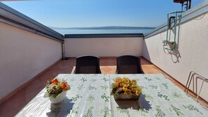 A balcony with a table and chairs, a flower arrangement, and a view of the sea. - Apartments Faran (Crikvenica)