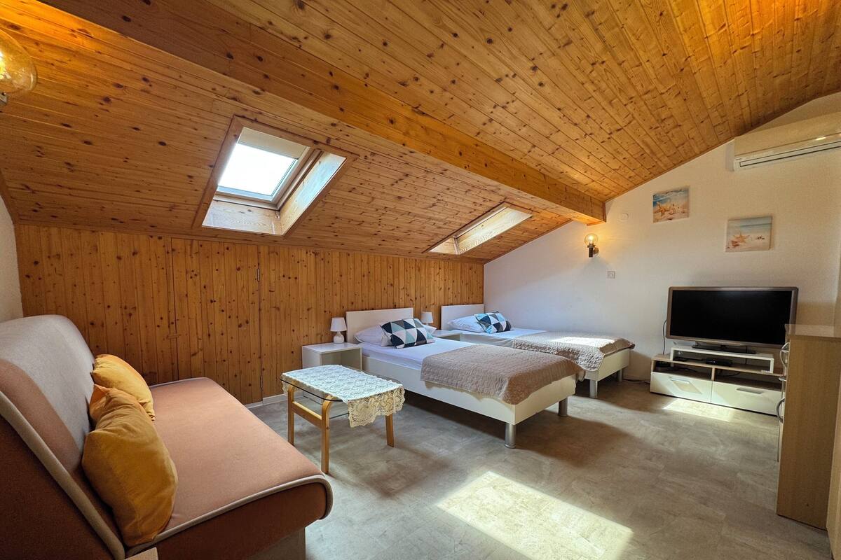 A cozy room with wooden walls, a sofa, two beds, a TV, and a skylight.