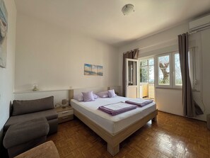 Ein Schlafzimmer mit Bett, Nachttisch, Kommode, Sofa und einem Fenster mit Vorhängen.