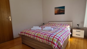 Ein Schlafzimmer mit Bett, Nachttisch, Schublade, einem Gemälde und einem Fenster mit Vorhängen.