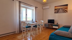 Ein Zimmer mit Holzboden, einem Schreibtisch mit Stühlen, einem Fernseher, einer Couch und einem Bild an der Wand.
