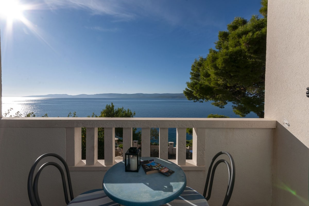 A balcony with a table, chairs, and a view of the sea.