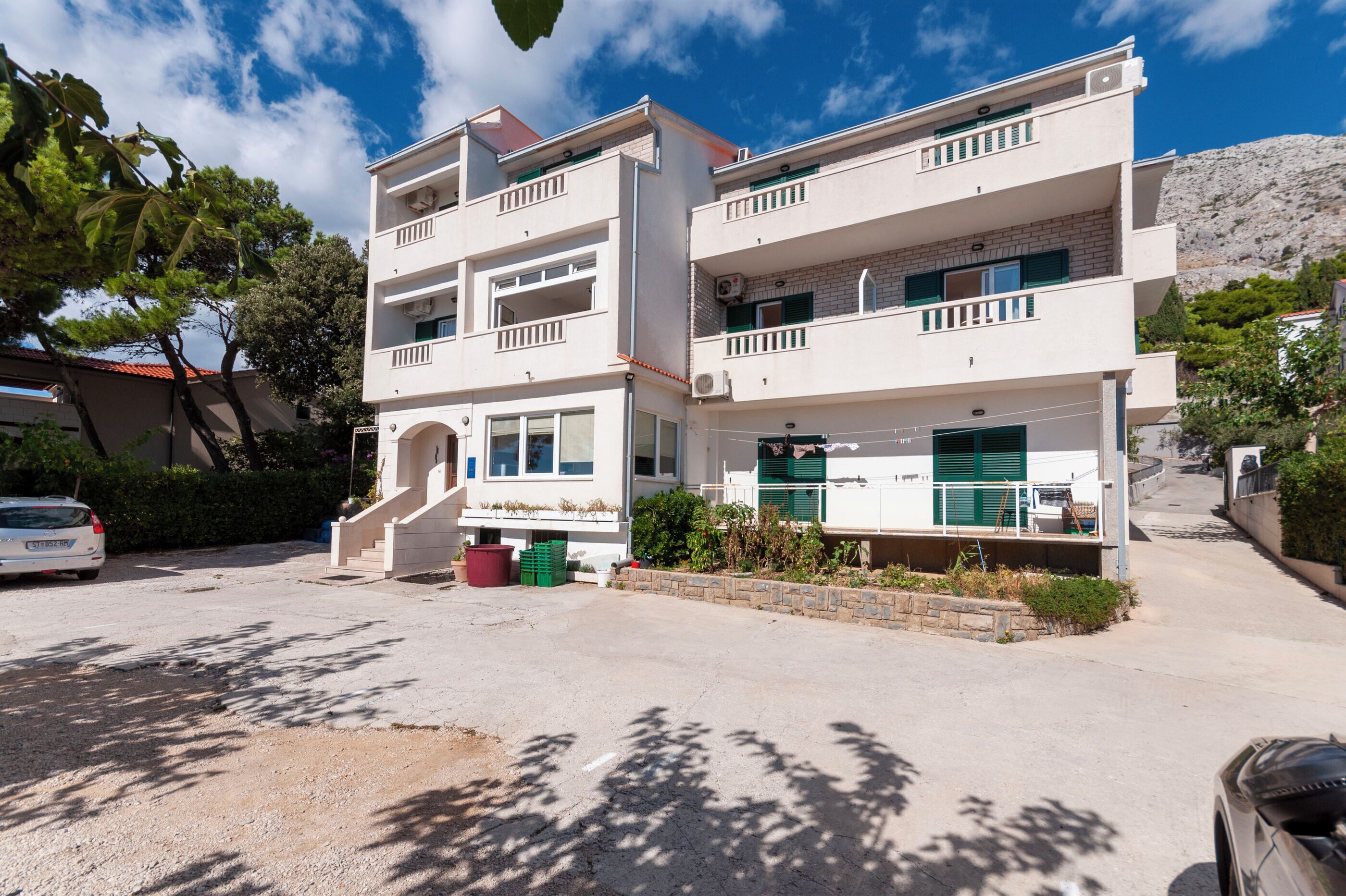 A two-story building with balconies, a driveway, and a parking area.