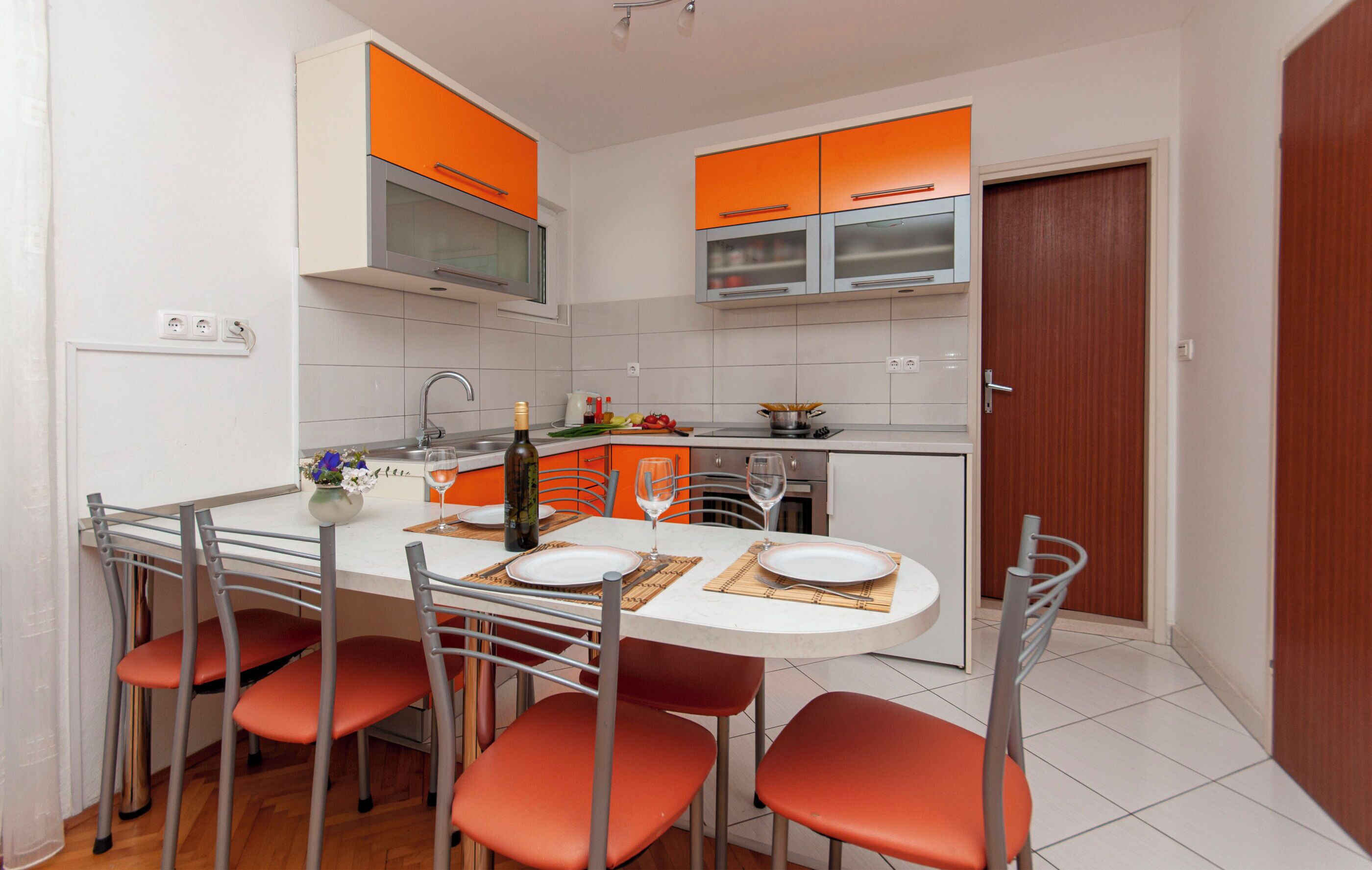 A compact kitchen with orange cabinets, a central island with seating, and a microwave above the sink.
