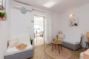 En moderne stue med en grå sofa, et rundt sofabord og udsigt gennem en åben dør til et spiseområde.