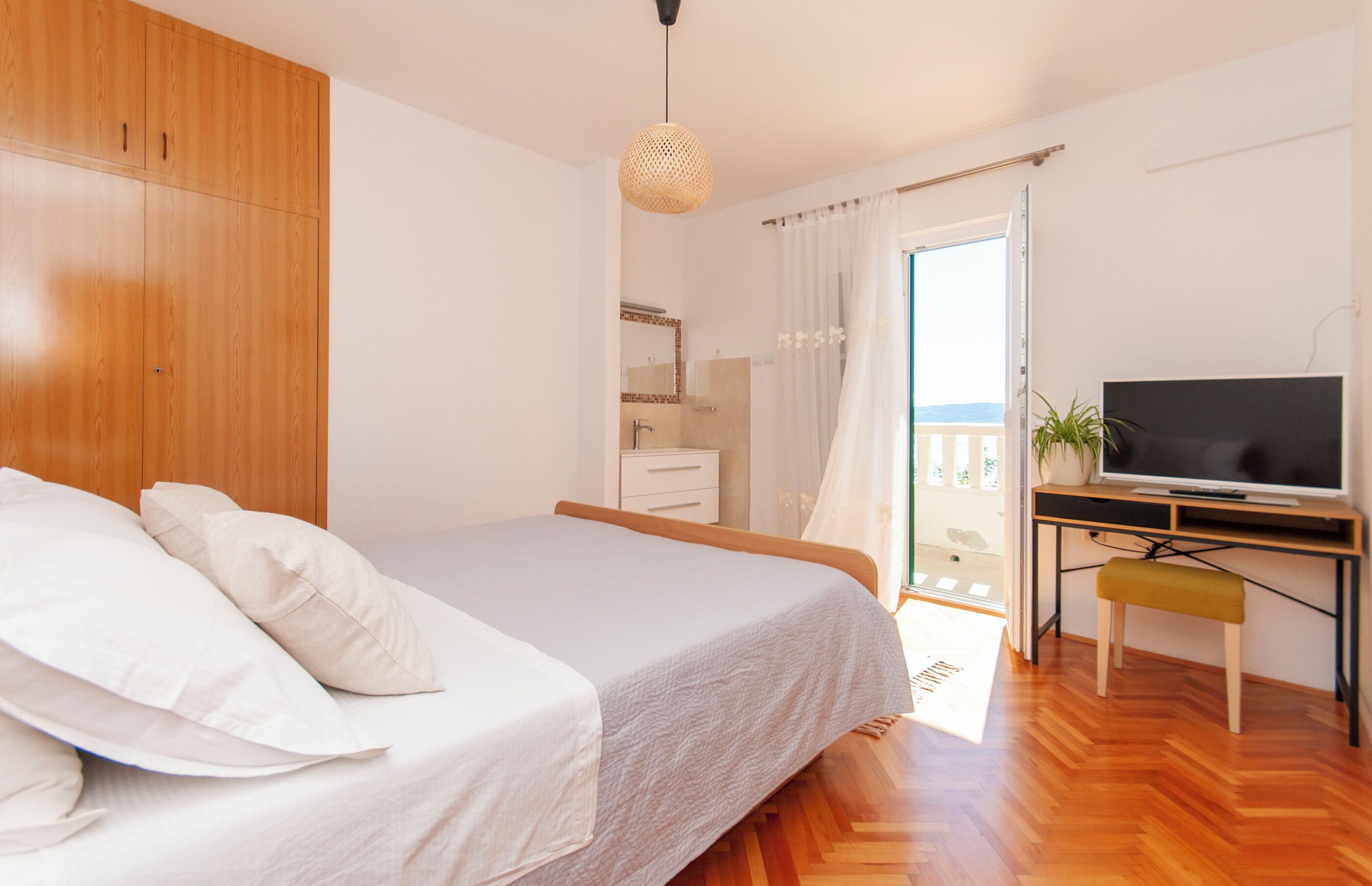 A bedroom with a bed, a TV, a desk, and a balcony with a view.