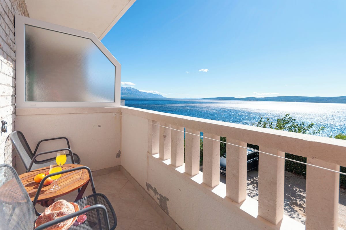A balcony with a table, chairs, and a view of the sea.