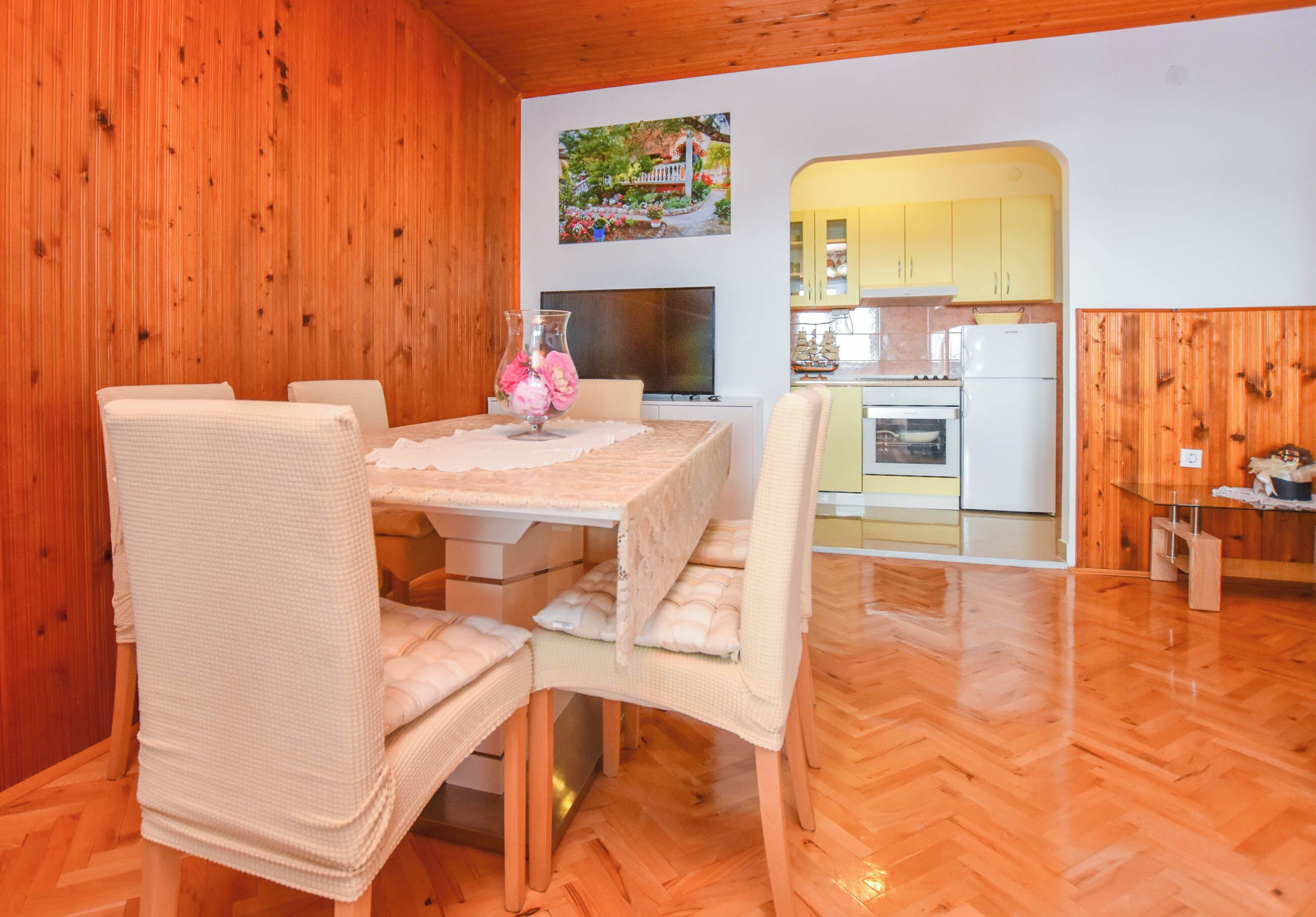 A dining area with a wooden interior, a TV, and a kitchen visible through an archway.