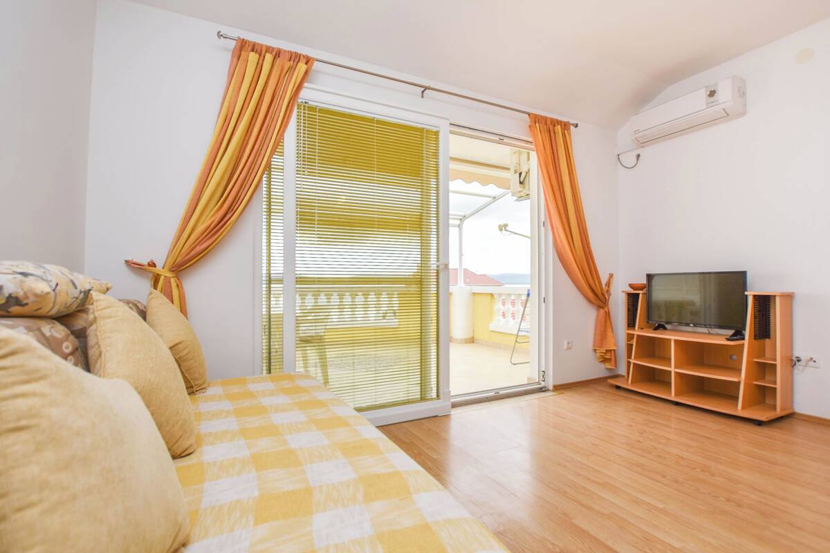 Une chambre avec un lit, un téléviseur posé sur un meuble en bois et une porte-fenêtre coulissante avec des rideaux.