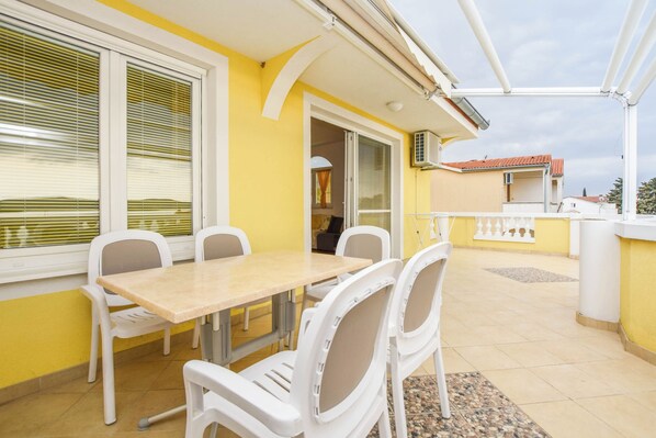 A balcony with a table and chairs, a sliding glass door, and a view of the neighboring buildings. - Apartments Dandelion (Biograd na Moru)