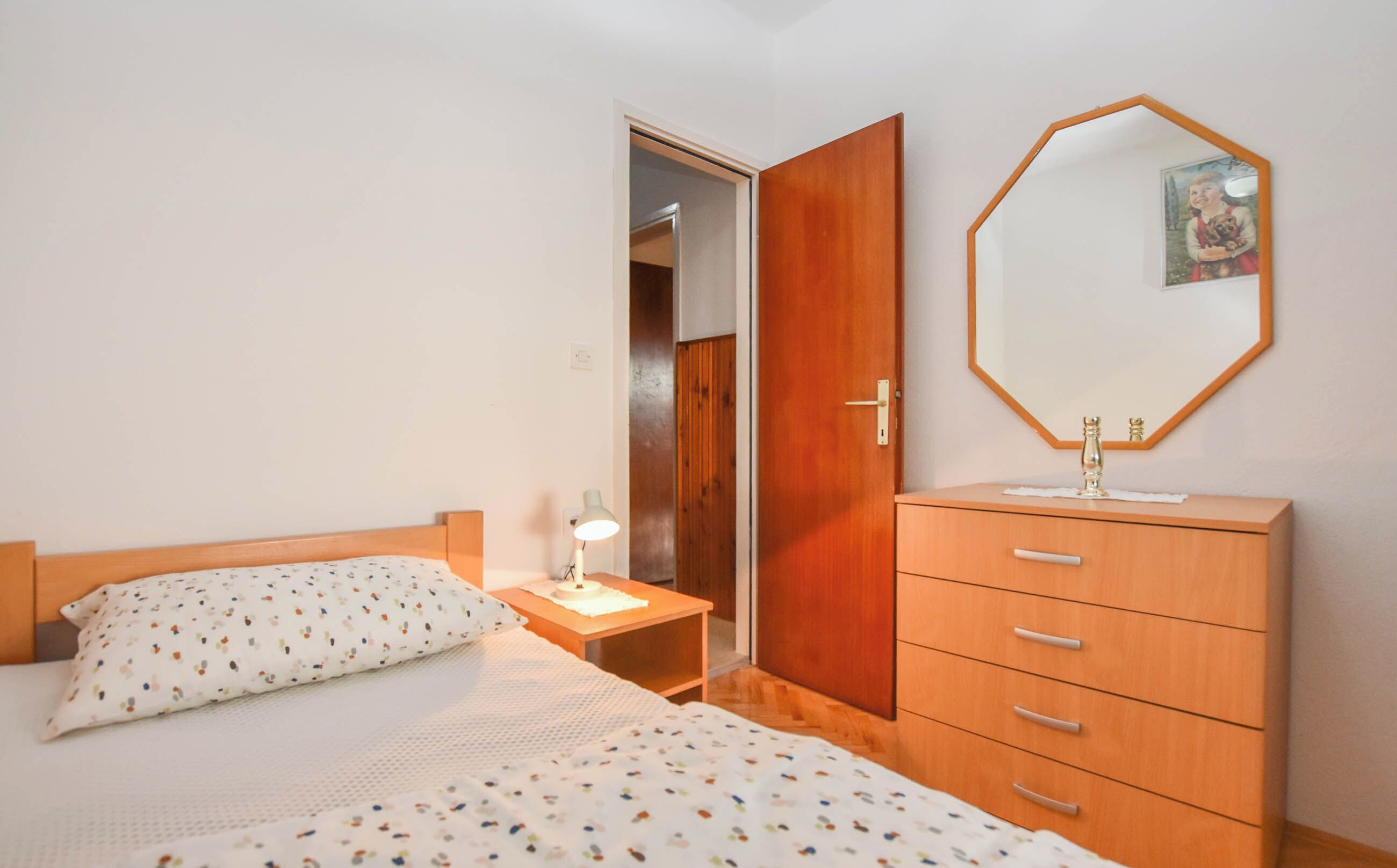 Een slaapkamer met een bed, nachtkastje, dressoir, spiegel en een deur naar een kast.