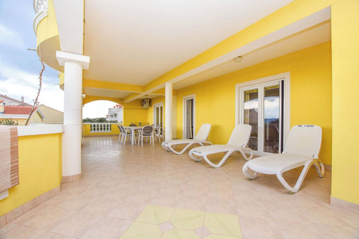 Un espace extérieur abrité, aux couleurs jaune et blanc, comprenant des chaises longues, une table et des chaises.