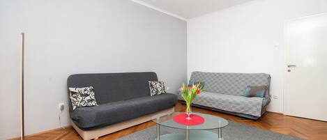A modern living room with a grey sofa, a patterned sofa, a glass coffee table, and a vase with flowers.