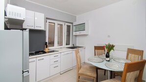 A modern kitchen with white cabinets, a built-in oven, and a dining area with a round table and chairs. - Apartment Kata (Sibenik)