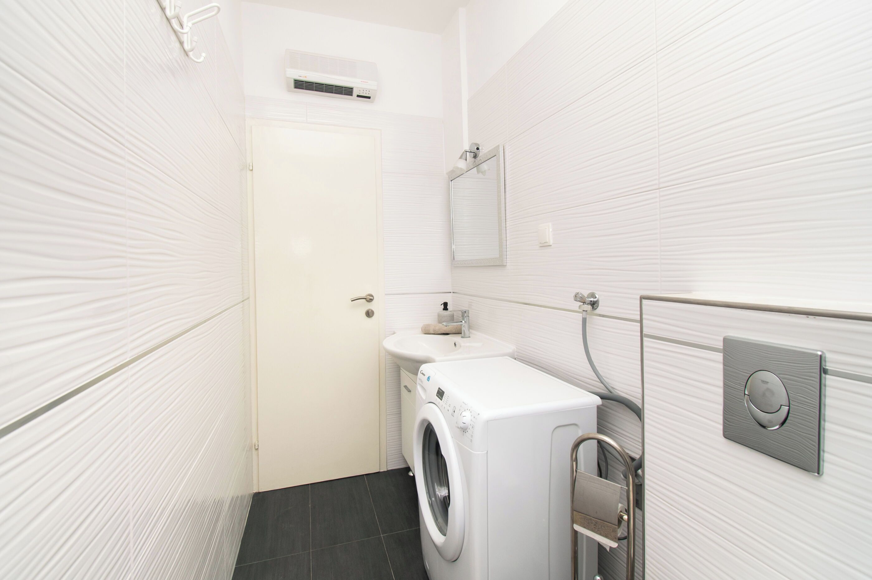 Een kleine, moderne badkamer met een ingebouwde wasmachine, een wastafel en een spiegel.