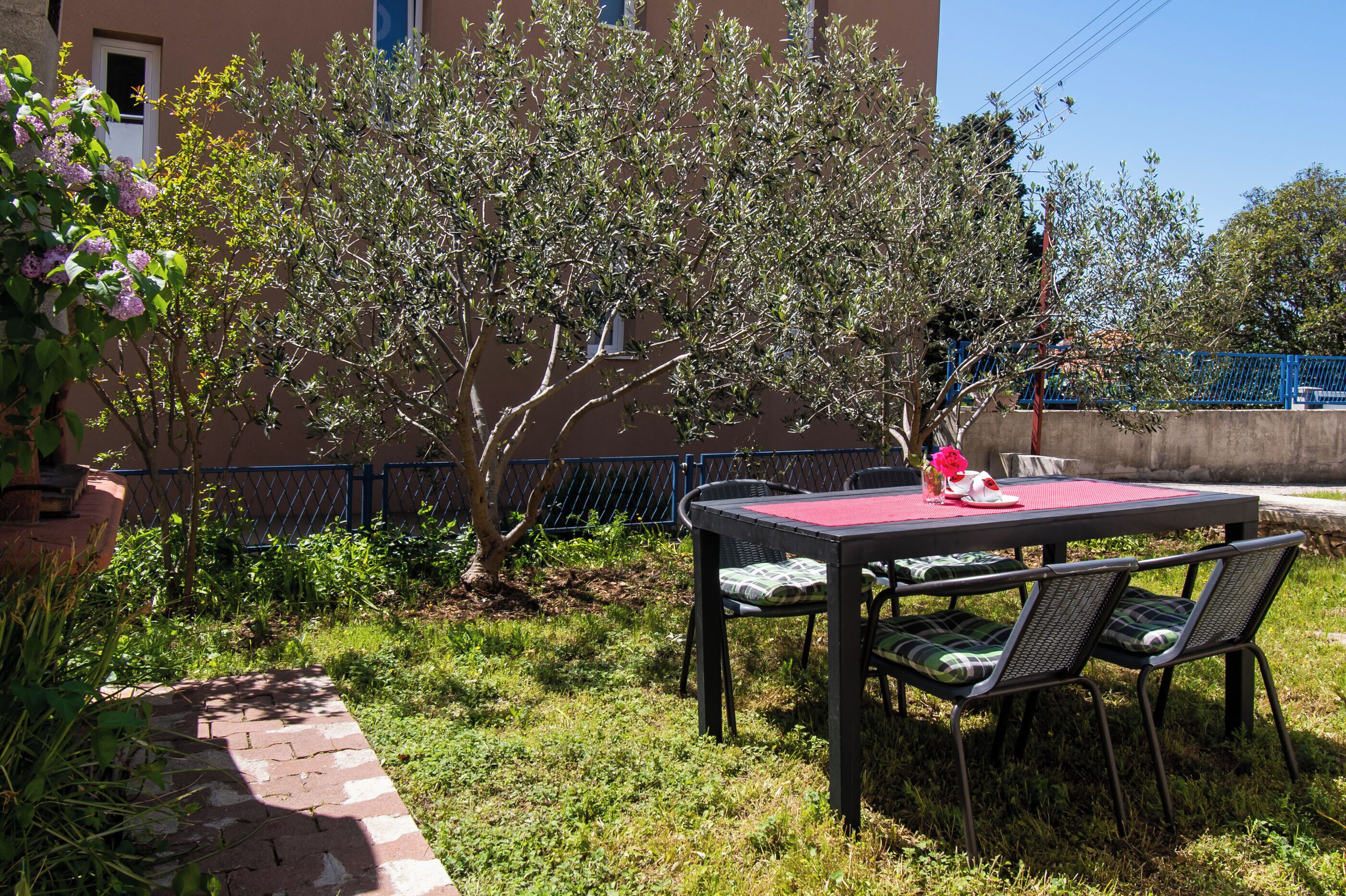Un patio al aire libre con una mesa y sillas, rodeado de follaje y un edificio al fondo.