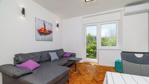 A modern living room with a grey sofa, a small table, and a window with a view of greenery. - Apartment Alej (Senj)