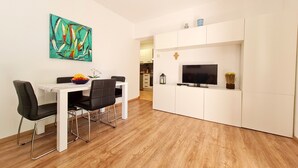 Un salon moderne comprenant un coin repas, des meubles blancs, un téléviseur à écran plat et une peinture abstraite aux couleurs vives.
