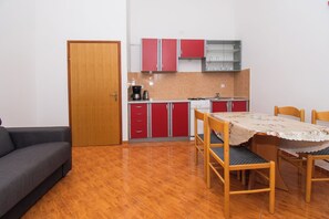 Eine kompakte Küche mit roten Schränken, einem Esstisch mit Stühlen und einer Couch.