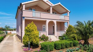 A two-story building with a balcony, a garden with various plants, and a clear sky. - Apartments Nikola (Nin)
