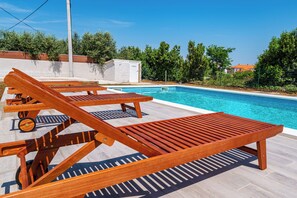 A poolside area with wooden lounge chairs and a clear blue pool. - Apartments Nikola (Nin)