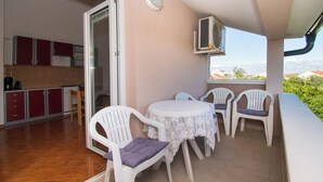 A balcony with a table and chairs, a kitchen area with cabinets, and an air conditioning unit. - Apartments Nikola (Nin)