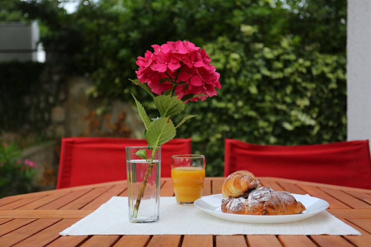 Une table avec un verre de jus d’orange, une pâtisserie et une fleur rose dans un vase.