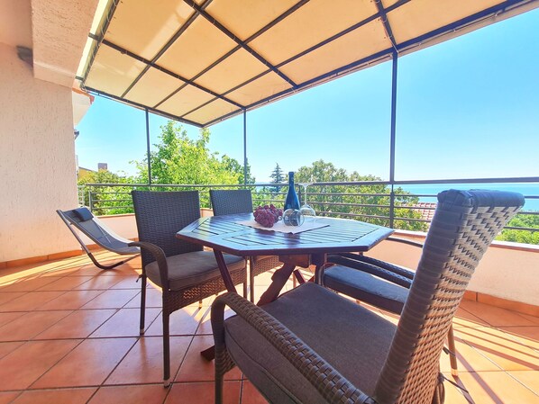 A covered outdoor seating area with a table and chairs, overlooking a scenic view. - Apartments Zelena Oaza (Novi Vinodolski)