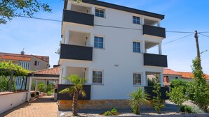 A multi-story building with balconies, a paved entrance, and surrounding greenery. - Apartments Jacqueline (Pakostane)