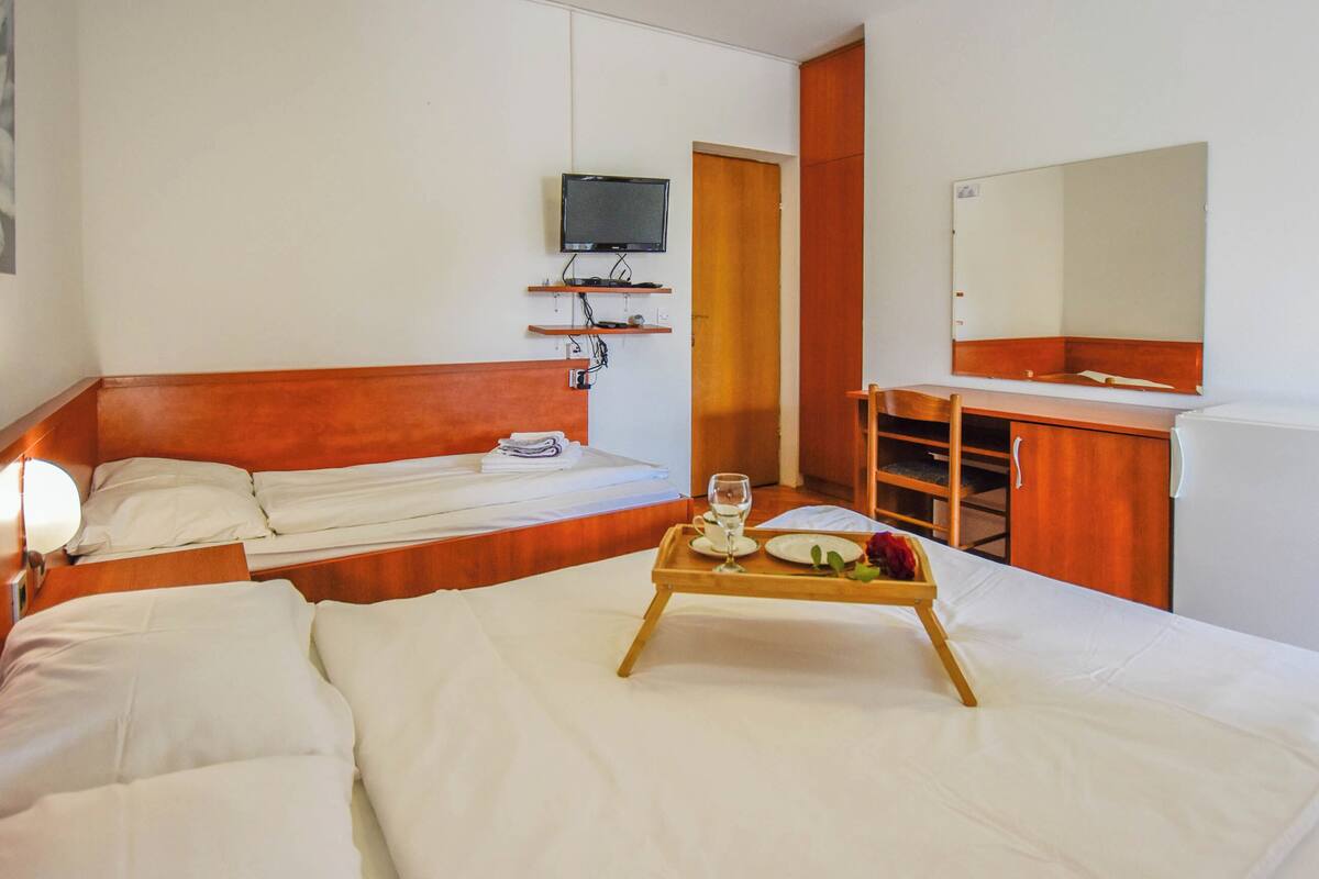 A hotel room with a bed, a desk, a television, and a tray with a glass of water and a plate of food.