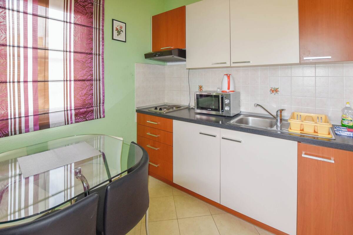 A compact kitchen with a microwave, sink, and a small dining area with a glass table and chairs.