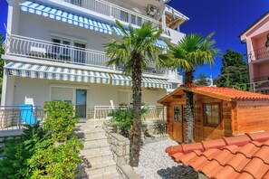 A multi-story building with balconies, a wooden cabin, and a stone pathway. - Apartment Blancas (Crikvenica)