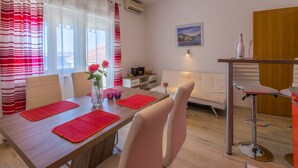 Un comedor con una mesa de madera, individuales rojos, sillas blancas y un jarrón con flores.