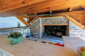 An attic-style kitchen with a brick fireplace, wooden beams, and a stone wall. - Apartment Blancas (Crikvenica)