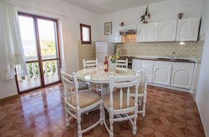Una cocina con armarios blancos, un refrigerador y una mesa de comedor con sillas.