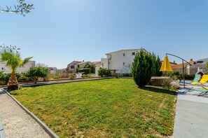 Zona residenziale con prato verde, piscina e ombrellone giallo.