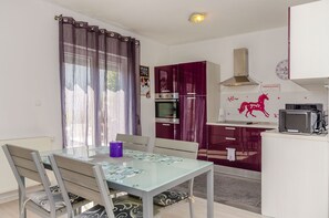 Una cucina compatta con forno a microonde, forno e un pensile rosso. Si trova un tavolo con sedie e una candela viola.