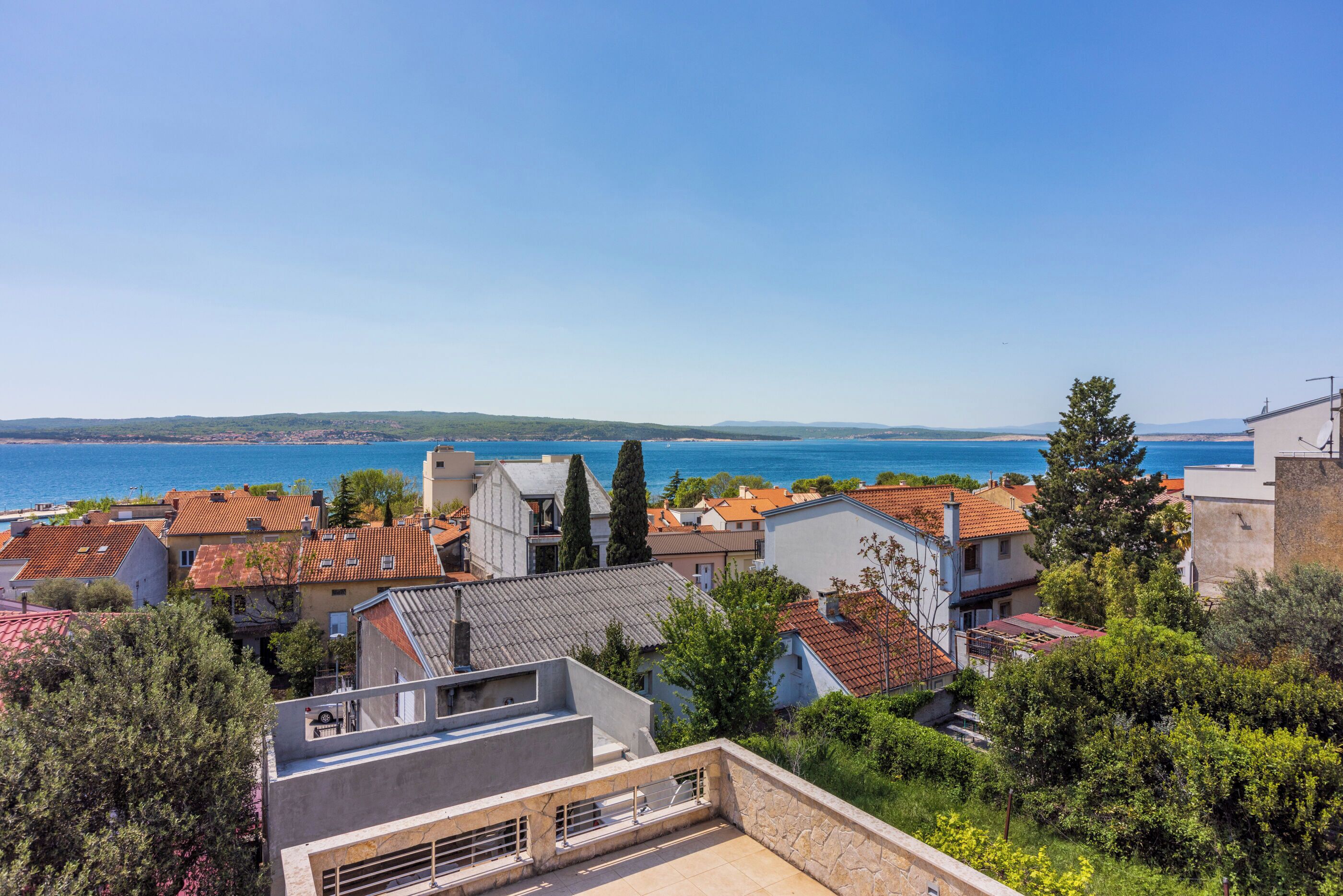 Ein Küstenwohngebiet mit Häusern mit Terrakotta-Dächern, blauem Himmel und Blick auf das Meer.