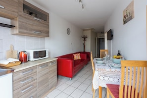 A compact kitchen with modern appliances, a red sofa, and a dining area with a table set for two. - Apartment Astrid (Crikvenica)