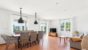 A spacious living area with a dining table, wicker chairs, a sofa, and a TV. - Villa Maite by Escape Home (Binibequer)