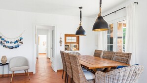 A dining area with a wooden table and wicker chairs, a black pendant light, and a white wall with a photo collage. - Villa Maite by Escape Home (Binibequer)