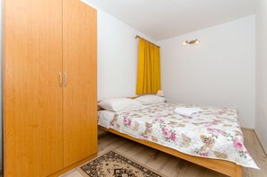 A bedroom with a wooden wardrobe, a bed with a floral bedspread, a yellow curtain, and a small wall-mounted light fixture. - Apartment Ane (Split)