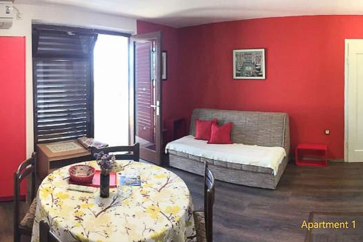 Un apartamento pequeño con zona de comedor, cama, kitchenette y una puerta roja.