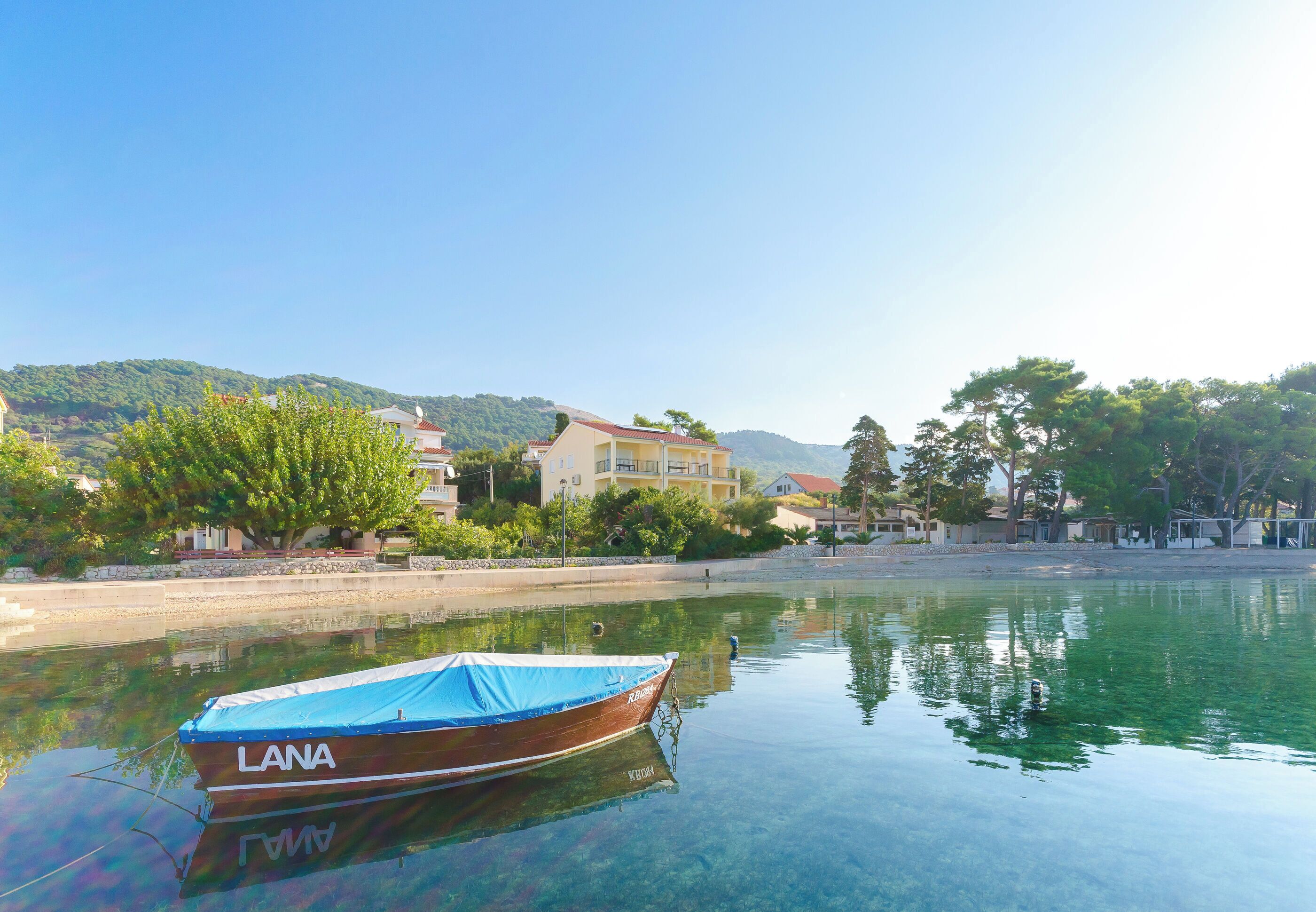 Un bateau nommé « LANA » était amarré dans une étendue d’eau calme, avec des bâtiments et de la végétation en arrière-plan.